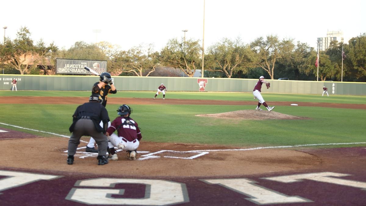 Batter raises his bat with pitcher mid-swing in the background on the Trinity baseball field